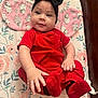 baby, child, red_clothing, black_headband, socks, floral_pattern, changing_pad, cute, infant, smiling, indoors, person, baby_girl, headwear, hand, footwear, fabric, soft_texture, wooden_furniture, comfort