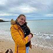 Ella participe au concours pour gagner de l'argent avec cette photo : woman, yellow_jacket, glasses, rabbit, dog, beach, sand, sea, cloudy_sky, waves, smile, casual_clothing, outdoor, pet, animal, nature, happy, leisure, water, coast