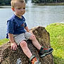 child, boy, rock, lake, water, fountain, grass, trees, outdoor, nature, shoes, shorts, tshirt, casual, sitting, daytime, sky, scenery, reflection, calm