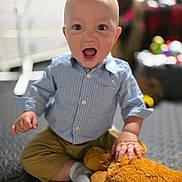 Abel is registered to the contest to win money with this photo: baby, child, indoor, smiling, happy, blue_shirt, striped, khaki_pants, stuffed_animal, plush_toy, sitting, floor, playful, cute, infant, portrait, hand, sock, expression, toy
