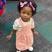 Daniela is registered to the contest to win money with this photo: child, toddler, girl, curly_hair, pink_bows, pink_dress, white_sneakers, carpet, arcade_game, indoor, portrait, standing, cute, fashion, play_area, person, young_child, looking_up, jewelry, innocent