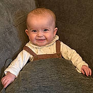 Emilia is registered to the contest to win money with this photo: baby, smiling, blanket, couch, infant, happy, child, face, clothing, sitting, indoors, cute, portrait, cozy, young_child, warm, comfort, person, baby_clothes, relax