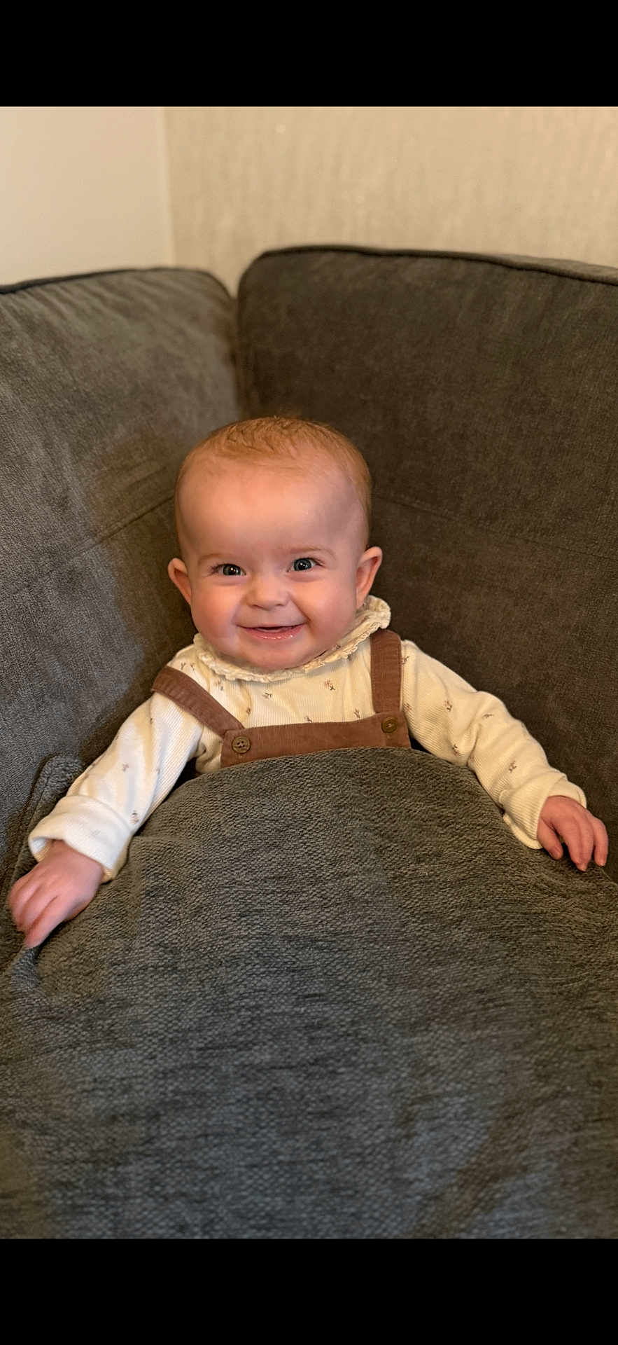 Emilia is registered to the contest to win money with this photo: baby, smiling, blanket, couch, infant, happy, child, face, clothing, sitting, indoors, cute, portrait, cozy, young_child, warm, comfort, person, baby_clothes, relax