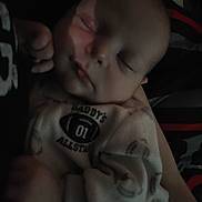 Owen is registered to the contest to win money with this photo: baby, infant, sleeping, closed_eyes, onesie, clothing, hand, arm, blanket, bed, pajamas, cute, portrait, indoor, dimly_lit, newborn, caregiver_arm, cuddle, infant_face, peaceful