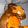 dog, stuffed_animal, plush_toy, brown_dog, orange_toy, snuggling, blanket, cozy, sleeping, cute, pet, fur, toy, indoor, relaxation, comfort, animal, cuddle, soft, rest