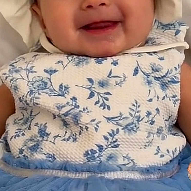 Mía is registered to the contest to win money with this photo: baby, child, infant, smiling, portrait, bonnet, dress, floral_pattern, blue_clothing, sitting, indoors, happy, face, eyes, mouth, fashion, baby_clothing, headwear, close_up, photography