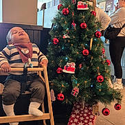 Saad joined the competition — help win amazing prizes! baby, child, high_chair, christmas_tree, christmas_decorations, red_baubles, gift_tags, indoor, cafe, floor_tiles, striped_sweater, bib, sleeping, wooden_furniture, person, holiday, festive, lights, present, people