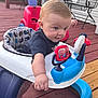 Anthony is registered to the contest to win money with this photo: baby, walker, toy, outdoor, deck, wooden_floor, curious, child, blue, red, plastic, seat, clothing, person, playtime, hands, foot, bench, metal, background