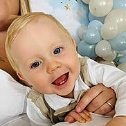 Amaël a rejoint le concours — aidez-le/la à gagner de superbes lots ! adult_hand, baby, balloons, beige_vest, blonde_hair, blue_eyes, celebration, child, close_up, cute, family, festive, happy, holding_hands, indoor, party, portrait, smiling, stars, white_shirt