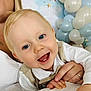 adult_hand, baby, balloons, beige_vest, blonde_hair, blue_eyes, celebration, child, close_up, cute, family, festive, happy, holding_hands, indoor, party, portrait, smiling, stars, white_shirt