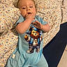 baby, blanket, blue_clothing, casual, child, cute, face, floor_tiles, footwear, hand_in_mouth, indoor, infant, lying_down, onesie, patterned_blanket, person, resting, skin, socks, teddy_bear_graphic