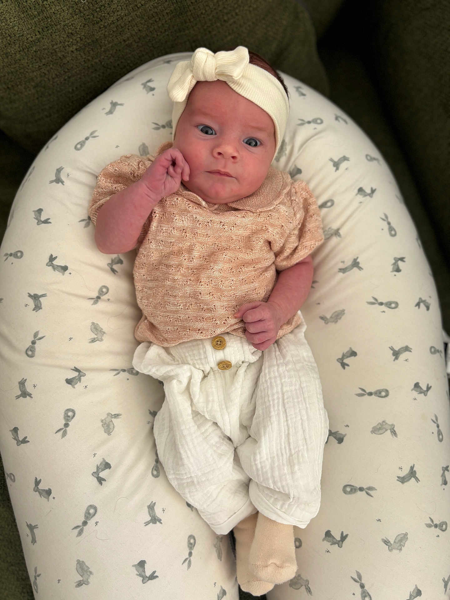 Lou a rejoint le concours — aidez-le/la à gagner de superbes lots ! baby, infant, headband, cushion, pattern, clothing, white_pants, socks, portrait, indoors, cute, soft_lighting, small_hands, relaxed, comfortable, expressive_face, newborn, neutral_background, seated, child