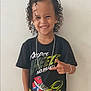 accessories, blackhair, child, clothing, curlyhair, dimples, face, female, footwear, girl, hair, happy, head, jewelry, necklace, person, shoe, sleeve, smile, t_shirt