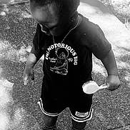 Kross is registered to the contest to win money with this photo: toddler, child, outdoor, hairbrush, black_and_white, tshirt, shorts, shoes, side_view, standing, shadow, sunlight, pavement, casual_clothing, necklace, curly_hair, person, young_child, summer, playful