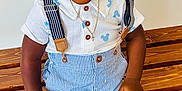 Kross is registered to the contest to win money with this photo: toddler, child, braided_hair, white_shirt, blue_shorts, striped_shorts, suspenders, wooden_bench, sandals, floor_tiles, necklace, gold_jewelry, earrings, curious_expression, indoor, portrait, smiling, sitting, brown_skin, casual_clothing