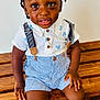 toddler, child, braided_hair, white_shirt, blue_shorts, striped_shorts, suspenders, wooden_bench, sandals, floor_tiles, necklace, gold_jewelry, earrings, curious_expression, indoor, portrait, smiling, sitting, brown_skin, casual_clothing