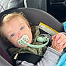 child, toddler, pacifier, car_seat, blanket, blue_eyes, clothing, seatbelt, car_interior, person, baby, sitting, head, face, sleeve, hand, hair, infant, safety, driver