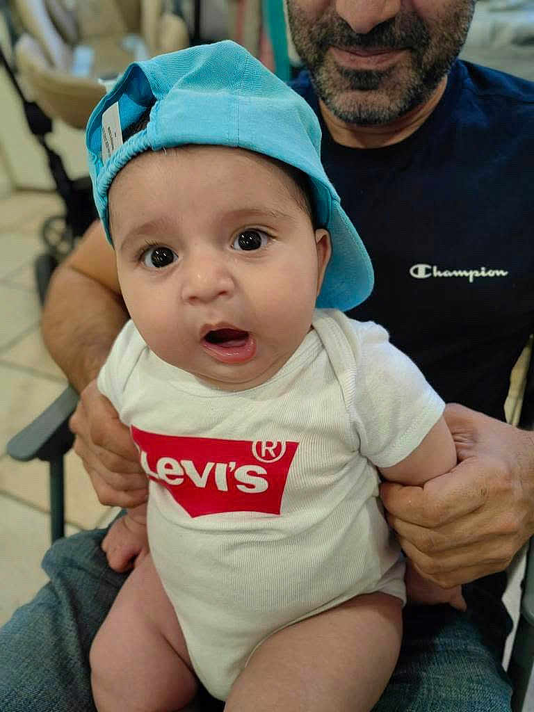 Aram participe au concours pour gagner de l'argent avec cette photo : baby, infant, child, blue_cap, onesie, levis_logo, adult, beard, champion_shirt, indoor, holding, seated, curious_expression, person, face, hand, casual_clothing, closeup, smiling, family