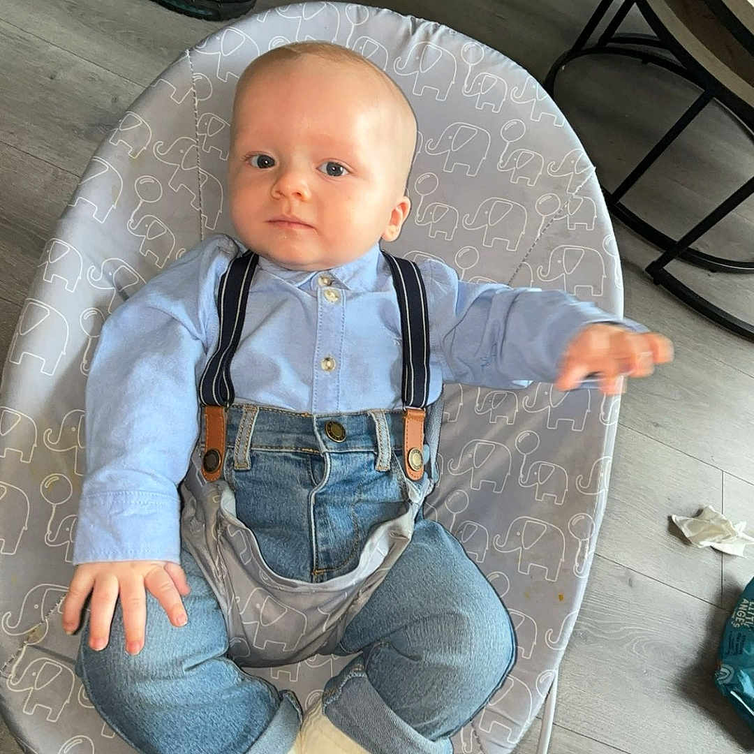 Oliver joined the competition — help win amazing prizes! adult_leg, baby, baby_seat, blue_shirt, casual_clothing, child, couch, curious, denim, elephant_pattern, floor, indoor, infant, living_room, overalls, person, sneaker, socks, table, wooden_floor
