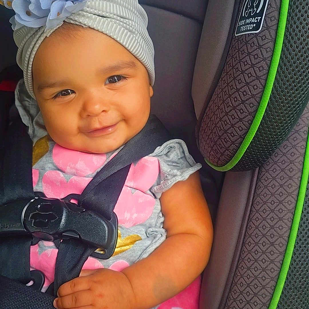 Mía Ahitana is registered to the contest to win money with this photo: baby, car_seat, child, clothing, cute, face, flower_headband, graco, gray, hand, happy, headwear, indoors, infant, pink, safety, seatbelt, sitting, smile, toddler