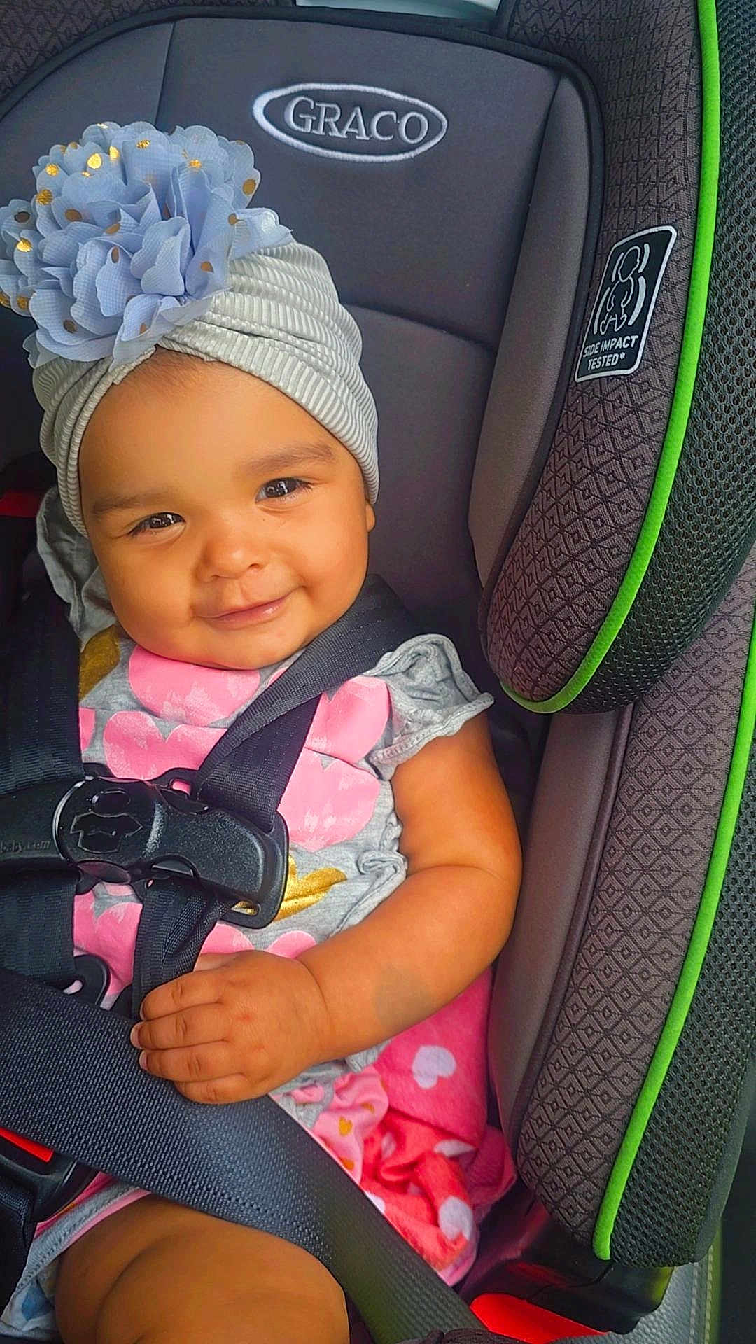 Mía Ahitana is registered to the contest to win money with this photo: baby, child, car_seat, graco, flower_headband, smile, seatbelt, infant, cute, sitting, clothing, pink, gray, hand, face, headwear, safety, toddler, indoors, happy