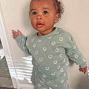 Camry is registered to the contest to win money with this photo: toddler, child, smiling_face, green_outfit, hair_bun, indoor, standing, wall, curious, expression, long_sleeve, pants, carpet, light, shadow, person, cute, young_child, apparel, portrait