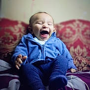 Austin joined the competition — help win amazing prizes! baby, infant, child, laughing, smiling, sitting, blue_clothing, pajamas, bed, bedspread, patterned_background, indoor, portrait, close_up, face, eyes_closed, open_mouth, happy, cozy, photograph
