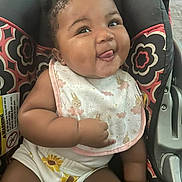 Serenity is registered to the contest to win money with this photo: baby, infant, car_seat, bib, clothing, cute, tongue_out, playful, patterned, sunflower, smile, child, adorable, seat, person, young, happy, face, skin, hair
