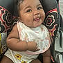 baby, infant, car_seat, bib, clothing, cute, tongue_out, playful, patterned, sunflower, smile, child, adorable, seat, person, young, happy, face, skin, hair