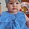baby, child, infant, portrait, blue_dress, hair_bow, headband, fashion, cute, serious_expression, face, eyes, indoors, restaurant, seated, close_up, photography, colorful_background, table, formalwear