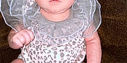 Semaj is registered to the contest to win money with this photo: baby, infant, child, onesie, leopard_print, frills, couch, brown, skin, feet, hands, face, eyes, sitting, indoors, portrait, cute, young, expression, person