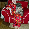 toddler, child, dog, puppy, red_pajamas, armchair, carpet, living_room, cushion, wooden_wall, family_photos, table, smiling, barefoot, indoor, cute, pet, cozy, home, furniture
