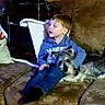 child, dog, couch, pillow, blanket, plaid, home_decor, indoors, pet, brown, blue_clothing, small_dog, snuggling, relaxed, cozy, seated, furniture, living_room, casual, portrait