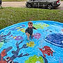 toddler, child, pool, water, splashing, sprinkler, outdoor, grass, car, house, play, summer, fun, colorful, water_toys, happy, sitting, nature, daylight, recreation