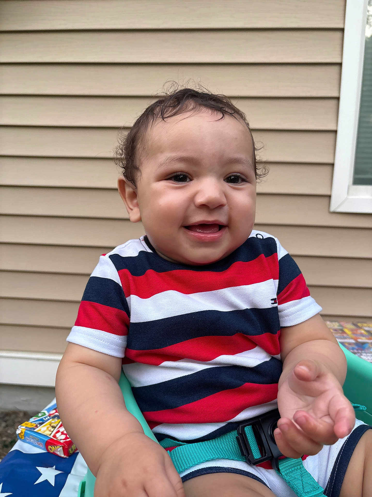 Michael is registered to the contest to win money with this photo: toddler, child, smiling, striped_shirt, curly_hair, outdoor, seat, green_seat, happy, baby, window, siding, arm, hand, casual_clothing, playful, portrait, young_child, daylight, person