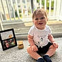 Carsen joined the competition — help win amazing prizes! baby, child, smiling, indoor, carpet, white_shirt, black_shorts, socks, framed_photo, wooden_box, sliding_door, glass, window, blurred_background, happy, cute, sitting, person, young_child, portrait
