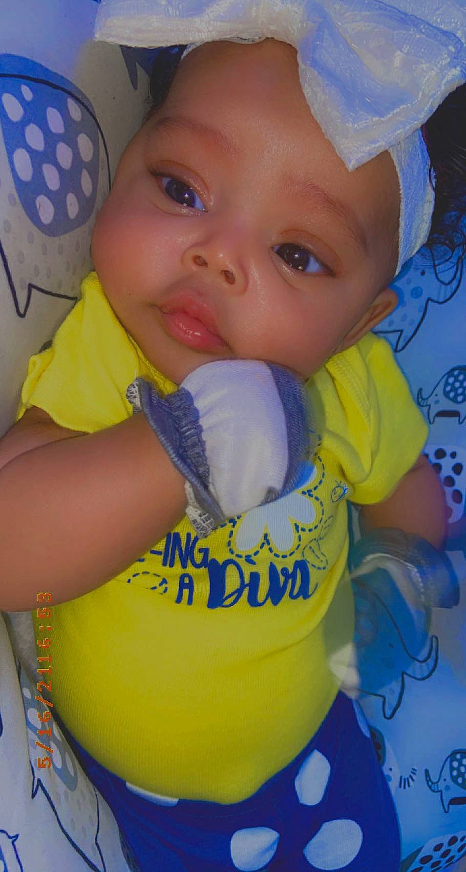 Ari is registered to the contest to win money with this photo: arm, baby, baby_playing_with_toys, baby_toddler_clothing, blue, cheek, child, dress, eye, face, finger, hand, happy, headgear, nose, person, skin, sleeve, toddler, white