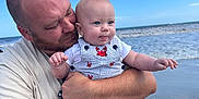 Matthew joined the competition — help win amazing prizes! baby, barefoot, beach, casual_clothing, child, clouds, family, happy, holding, man, nature, ocean, outdoor, person, red_crab_pattern, short_sleeve, sky, smile, striped_overalls, water