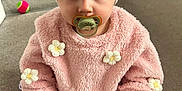 Mayva joined the competition — help win amazing prizes! baby, child, pacifier, headband, flower, pink_sweater, carpet, toy, indoor, sitting, cute, infant, clothing, white_socks, daisy, hand, face, eyes, floor, adorable