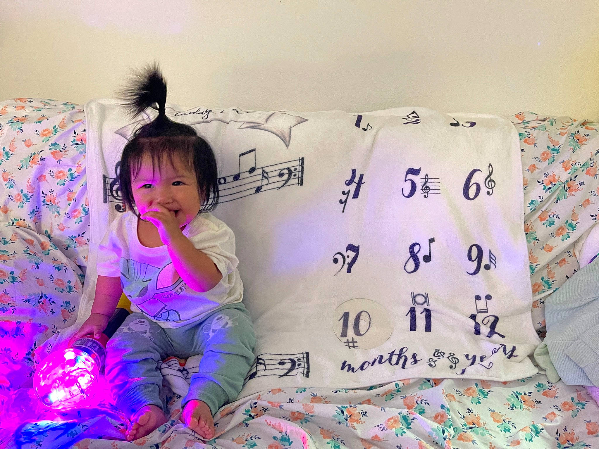 John Mason is registered to the contest to win money with this photo: baby_toddler_clothing, bed, bed_sheet, bedding, bedroom, comfort, font, happy, linens, magenta, pattern, person, pillow, pink, purple, sitting, sleeve, textile, throw_pillow, toddler