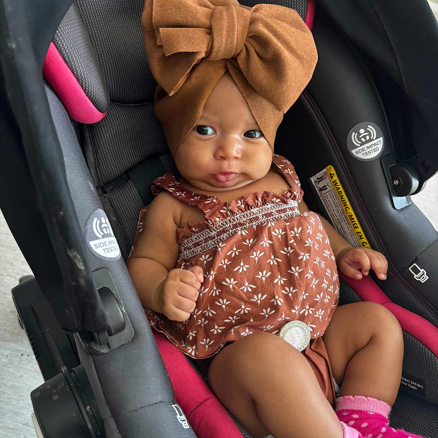 Elliani joined the competition — help win amazing prizes! baby, bow, car_seat, child, closeup, cute, dress, expression, footwear, hands, headwrap, indoor, infant, legs, patterned_clothing, person, pink_socks, portrait, seat_belt, small_child
