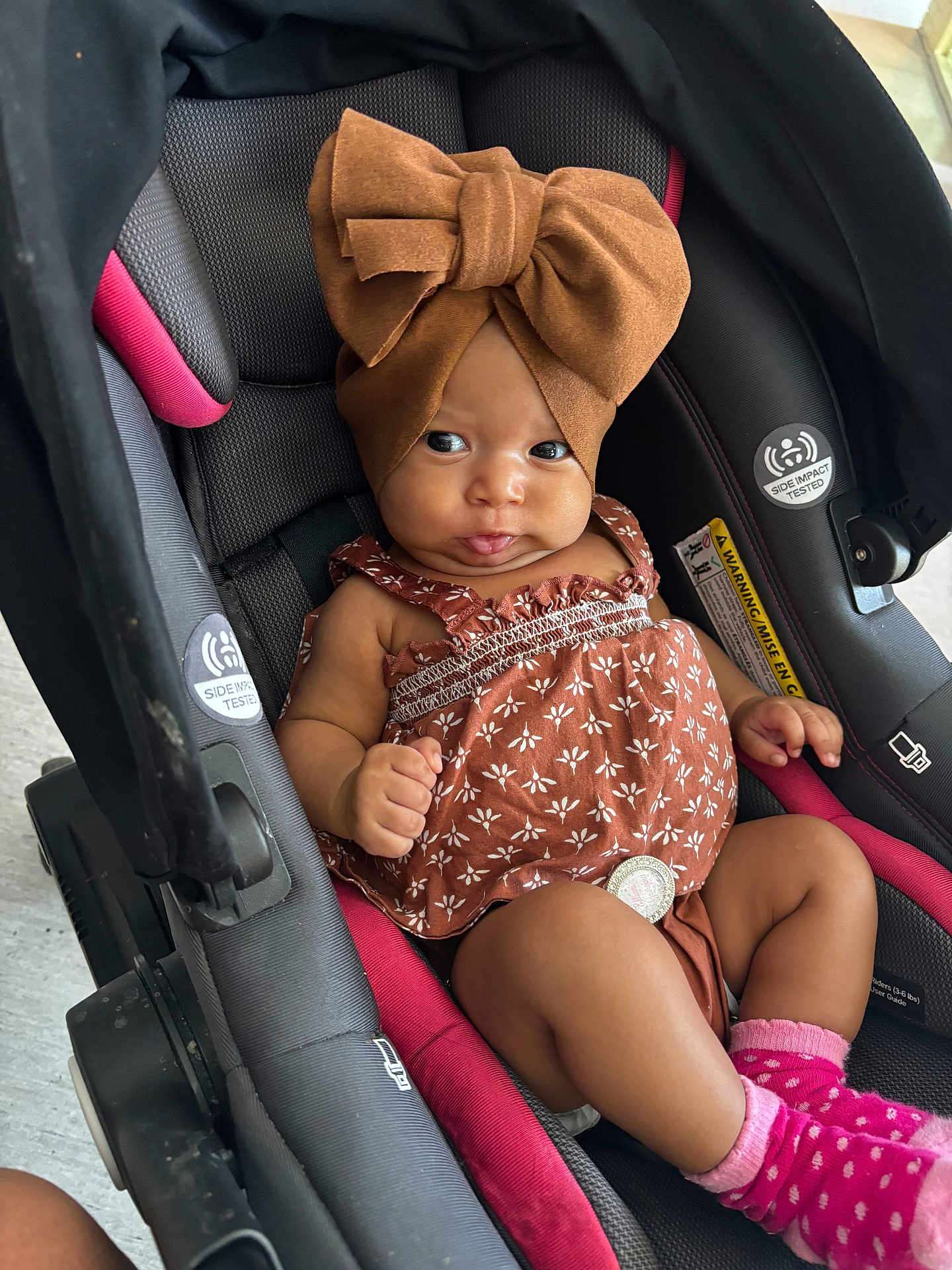 Elliani joined the competition — help win amazing prizes! baby, car_seat, headwrap, bow, dress, pink_socks, infant, child, seat_belt, patterned_clothing, cute, indoor, portrait, person, small_child, hands, legs, footwear, expression, closeup