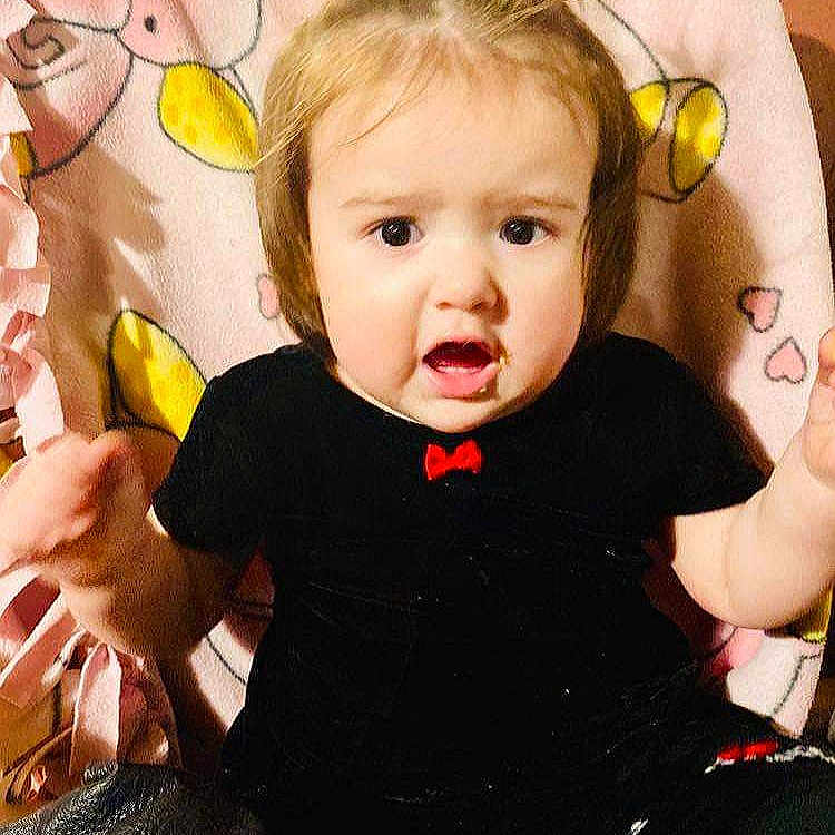 Ezalyn is registered to the contest to win money with this photo: animal_pattern, baby, black_clothing, blanket, cartoon, child, curious, cute, expression, face, hair, hands, indoor, person, pigtails, pink_blanket, red_bow, sitting, snack, toddler