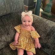 Margueritte is registered to the contest to win money with this photo: baby, bow, child, couch, decor, dress, floral_dress, happy, headband, infant, legs, living_room, person, portrait, sitting, smile, socks, sofa, vase, wood_paneling