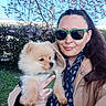 blossom_tree, blue_sky, coat, dog, grass, hedge, holding, jewelry, leash, outdoors, owner, park, pomeranian, portrait, puppy, scarf, smiling, sunglasses, timestamp, woman
