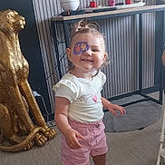Lyha a rejoint le concours — aidez-le/la à gagner de superbes lots ! candles, cheetah, child, eye_patch, flooring, golden_statue, hair_tied, happy, home_decor, indoor, person, pink, playful, rug, sandals, shorts, smile, table, toddler, white_shirt