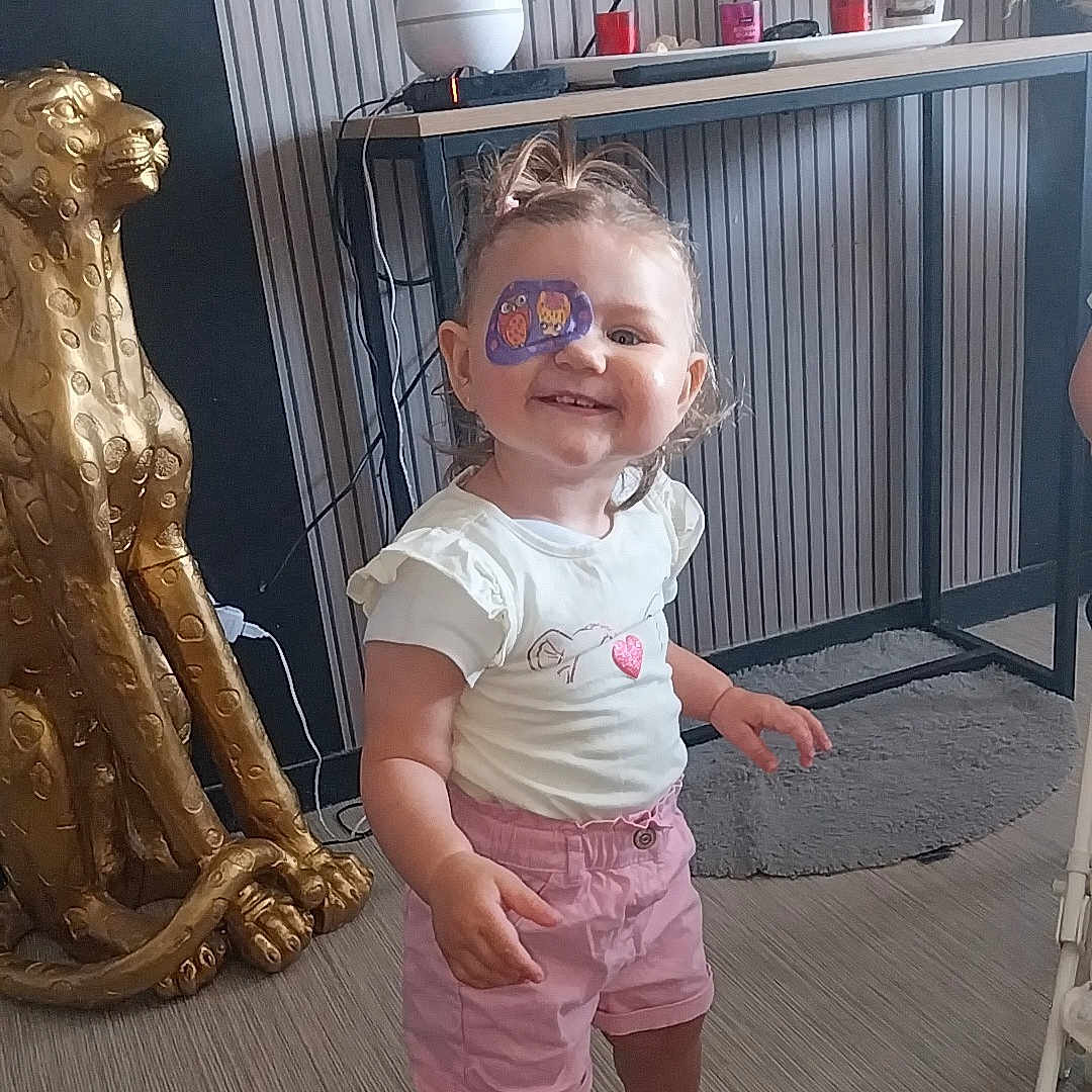 Lyha a rejoint le concours — aidez-le/la à gagner de superbes lots ! candles, cheetah, child, eye_patch, flooring, golden_statue, hair_tied, happy, home_decor, indoor, person, pink, playful, rug, sandals, shorts, smile, table, toddler, white_shirt