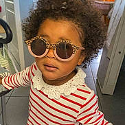 Ariane participe au concours pour gagner de l'argent avec cette photo : toddler, child, sunglasses, striped_clothing, red_dress, curly_hair, indoor, floor_tiles, door, light, window, home, furniture, walker, person, fashion, playful, cute, portrait, young_child