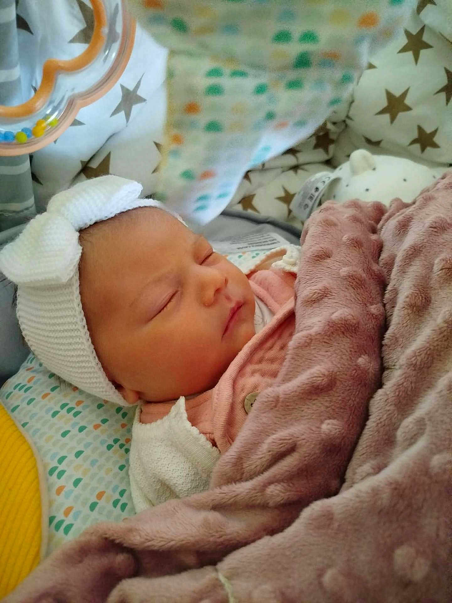 Romy participe au concours pour gagner de l'argent avec cette photo : baby, sleeping, blanket, headband, bow, cushion, patterned, soft, toy, infant, cozy, pink, white, clothing, face, peaceful, rest, indoor, portrait, child