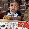 child, toddler, girl, portrait, restaurant, dining, menu, food, tortilla_chip, snack, chair, table, brick_wall, indoor, sitting, curly_hair, hair_bows, looking_at_camera, facial_expression, family
